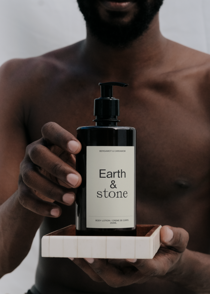 Man holding black bottle with label Earth & Stone, mockup for body lotion packaging design, clear branding, visual identity, skincare product.